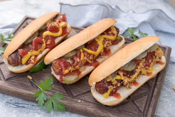 Hot Dog mit Speckwürstchen, Ketchup, gelbem Senf, gebratenen Zwiebeln und Essiggurken — Stockfoto