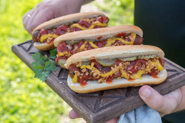 Hot Dog mit Speckwürstchen, Ketchup, gelbem Senf, gebratenen Zwiebeln und Essiggurken — Stockfoto