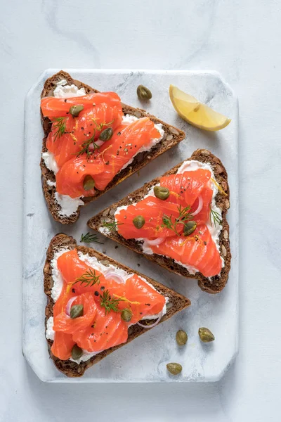 Smorrebrod, traditionele Deens open sanwiches, donker roggebrood met zalm, room kaas en kappertjes. — Stockfoto