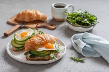 Kruvasan sandviç sahanda yumurta, salata yaprakları ve avokado ile Kahvaltı