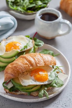Kruvasan sandviç sahanda yumurta, salata yaprakları ve avokado ile Kahvaltı