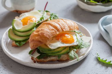 Kruvasan sandviç sahanda yumurta, salata yaprakları ve avokado ile Kahvaltı