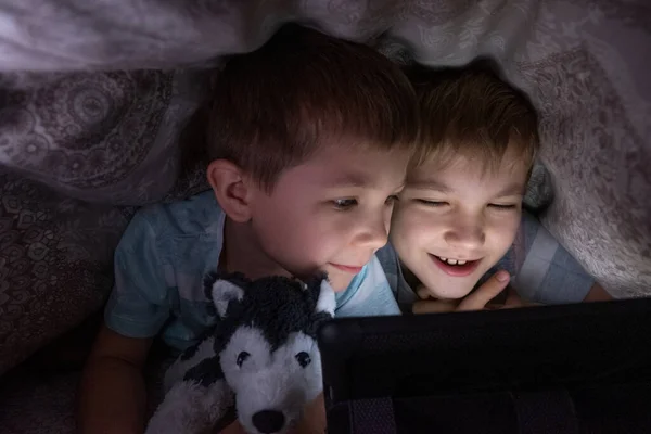Bröder barn med surfplatta dator under filt — Stockfoto