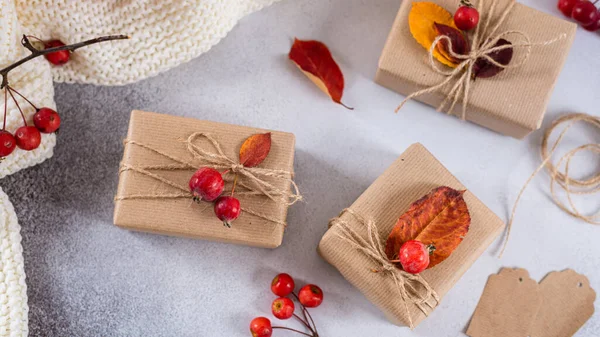 Autumn vibes, thanksgiving day presents, seasonal sale concept. Fall composition with presents in craft paper decorated with dried leaves and red berries on gray background. Top view