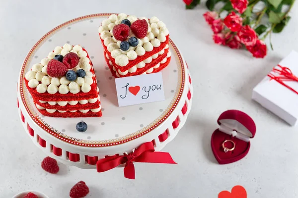 Romantic present on St. Valentines Day. Two cakes in heart shape, roses bouquet and a gift box with a ring on light background. Selective focus