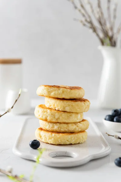 Cottage cheese pancakes on a white background. Syrniki with fresh blueberries. Pancakes with cottage cheese on a white board sprinkled with powdered sugar. Homemade food. Recipe. Copy space for text