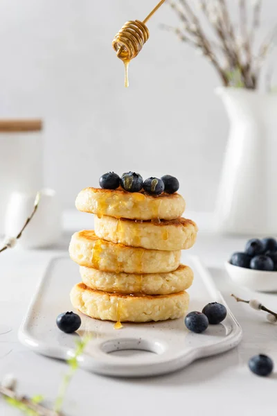 Cottage cheese pancakes with fresh blueberries and honey. Russian syrniki or sirniki, cottage cheese fritters or pancakes served with berries. Restaurant menu, cookbook recipe. Side view