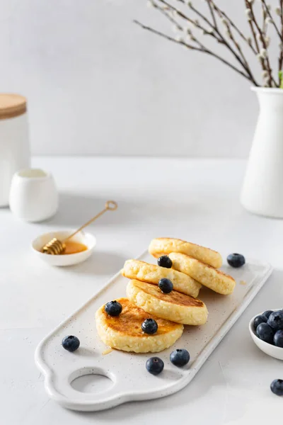 Cottage cheese pancakes with fresh blueberries and honey. Russian syrniki or sirniki, cottage cheese fritters or pancakes served with berries. Restaurant menu, cookbook recipe. Copy space for text