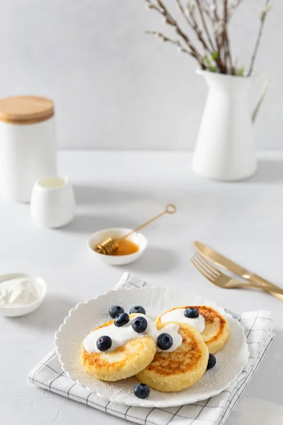 Cottage cheese pancakes with fresh blueberries and honey. Russian syrniki or sirniki, cottage cheese fritters or pancakes served with berries. Restaurant menu, cookbook recipe. Side view