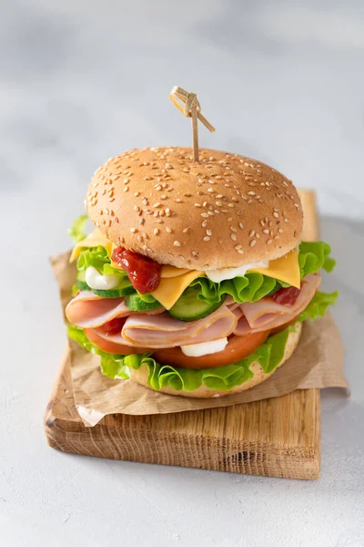 Delicious sandwich with fresh vegetables, cheese and ham on wooden board on gray background. Side view, close up, vertical. Menu, recipe