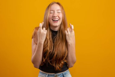 Kazanmak zorundayım. Neşeli genç kızıl kadın dişlerini sıkar, parmaklarını çapraz yapar, arzulanan dilekleri yapar, kıvırcık saçlar, melez ırk, beyaz kız, iyi haberleri bekler, sarı duvarın üzerinde durur..