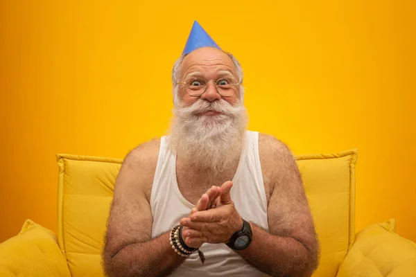 Positive elderly man in party hat smiling to camera, birthday celebration