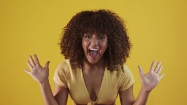 Genç Brezilyalı kıvırcık kadın sarı arka planda hareketli ve poz veriyor