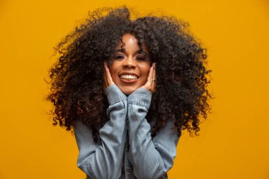 Afro saç stili ve cazibeli makyajlı Afro-Amerikan kadının güzel portresi. Brezilyalı kadın. Karışık ırk. Kıvırcık saçlı. Saç stili. Sarı arkaplan.