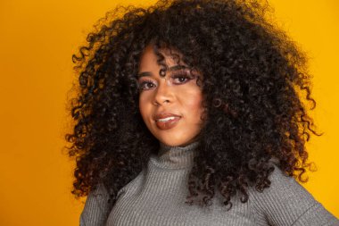 Afro saç stili ve cazibeli makyajlı Afro-Amerikan kadının güzel portresi. Brezilyalı kadın. Karışık ırk. Kıvırcık saçlı. Saç stili. Sarı arkaplan.