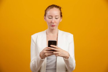 Genç, kendine güvenen, başarılı ve güzel iş kadını sarıda akıllı telefonu olan kızıl saçlı kadın. Meslek, kariyer, iş kavramı.