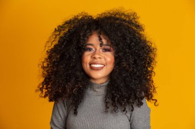 Afro saç stili ve cazibeli makyajlı Afro-Amerikan kadının güzel portresi. Brezilyalı kadın. Karışık ırk. Kıvırcık saçlı. Saç stili. Sarı arkaplan.