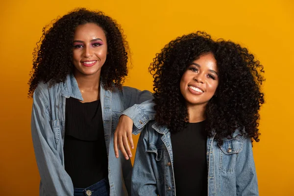 Two young afro-american women with curly hair looking at camera and smiling. Cute afro girls with curly hair smiling looking at camera.