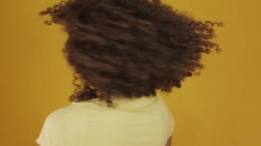 Genç Brezilyalı kıvırcık kadın sarı arka planda hareketli ve poz veriyor