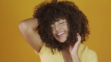 Genç Brezilyalı kıvırcık kadın sarı arka planda hareketli ve poz veriyor