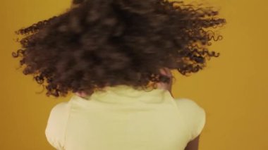 Genç Brezilyalı kıvırcık kadın sarı arka planda hareketli ve poz veriyor