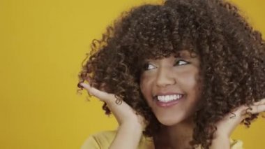 Genç Brezilyalı kıvırcık kadın sarı arka planda hareketli ve poz veriyor