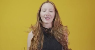 Sarı arka planda el kol hareketi yapan kızıl saçlı genç kadın.