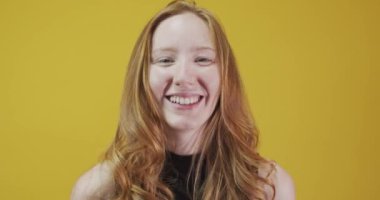 Sarı arka planda el kol hareketi yapan kızıl saçlı genç kadın.