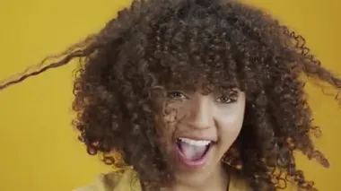 Genç Brezilyalı kıvırcık kadın sarı arka planda hareketli ve poz veriyor