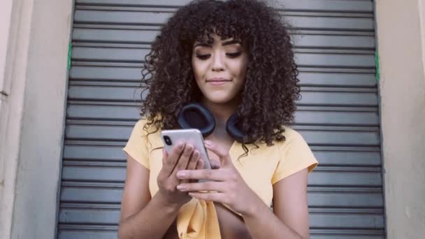 Κομψό Σγουρά Γυναίκα Χρησιμοποιώντας Smartphone Που Θέτουν Φόντο Της Πόλης — Αρχείο Βίντεο