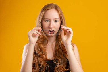 Güzel kızıl saçlı, kıvırcık saçlı, gözlükleriyle mutlu bir kadın. Göz bakımı konsepti. Sarı arkaplanda.