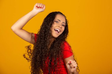 Genç, güzel, kıvırcık saçlı, kıvırcık saçlı kız sarı arka planda mutlu bir şekilde evet diyor. Başarı ve başarı kavramı. Sarı arka planda neşeli, güzel bir kadın.