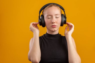 Mutlu ve kaygısız heyecanlı hippi kız yeni kulaklıkları gibi, elleri havada dans ediyor ve gülümsüyor turuncu arka planda müzik dinlemenin keyfini çıkarıyor, en sevdiği şarkıyla ruh halini yükseltiyor..