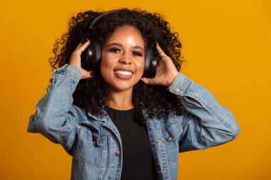 İnsanlar, müzik, duygu konsepti. Afro saç stili ile zevkli bir kadın melodi ile dans ediyor, gözlerini kapatıyor kulaklıkla yüksek sesle şarkı dinliyor. Kulaklıklı, güzel afro bir kadın.