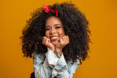 Afro saç stili ve cazibeli makyajlı Afro-Amerikan kadının güzel portresi. Brezilyalı kadın. Karışık ırk. Kıvırcık saçlı. Saç stili. Sarı arkaplan.