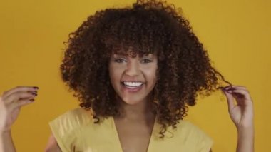 Genç Brezilyalı kıvırcık kadın sarı arka planda hareketli ve poz veriyor