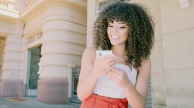 Şehrin arka planında akıllı telefon kullanan şık kıvırcık kadın.