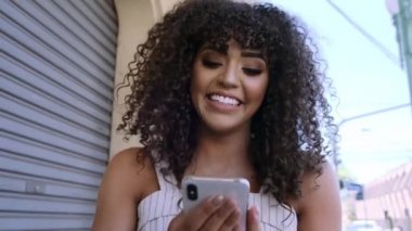 Şehrin arka planında akıllı telefon kullanan şık kıvırcık kadın.