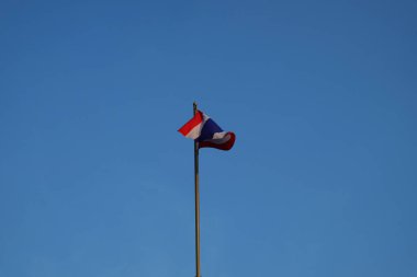 Tayland bayrağı mavi gökyüzüne karşı bayrak direğinde dalgalanıyor..