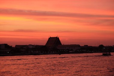 Bangkok 'taki Chao Phraya Nehri üzerinde inanılmaz bir gün batımı. Nehir kenarındaki binaların siluetleri.