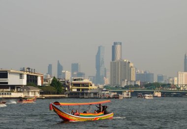Bangkok, Tayland, 26 Aralık 2018. İnsanlar Chao Phraya nehri boyunca çok renkli küçük bir tekneyle modern gökdelenlerin arka planına doğru yol alıyorlar..