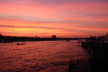Bangkok 'taki Chao Phraya Nehri üzerinde inanılmaz bir gün batımı. Nehir kenarındaki binaların siluetleri.