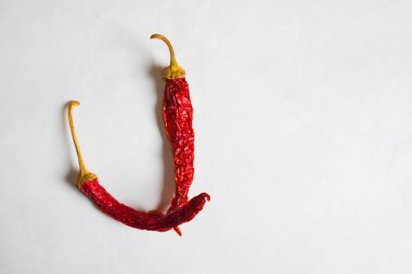 J harfi beyaz arka planda kırmızı biberlerle kaplanmış. J harfinde J. Pepper harfi şeklinde beyaz bir arkaplan üzerine çizilmiş sembol..