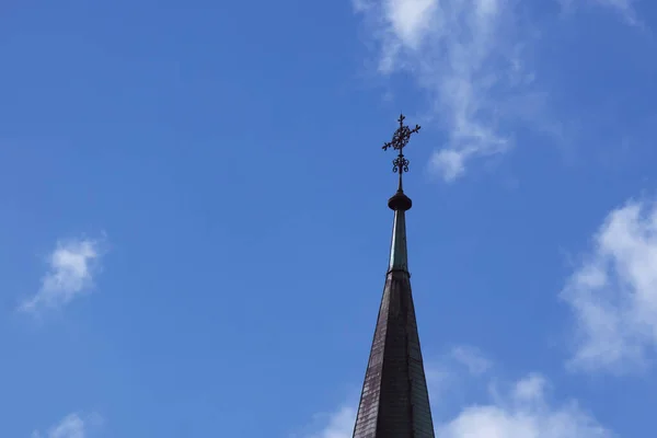 The spire of the Christian church with a cross on a background of blue sky.