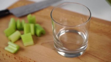 Taze sıkılmış kereviz suyu, tahta kesme tahtasındaki cam bardağa dökülüyor. Bir bıçak ve dilimlenmiş sulu dilimlerle. Yukarıdan bak. Diyet hazırlığı ve temizlik içecekleri.