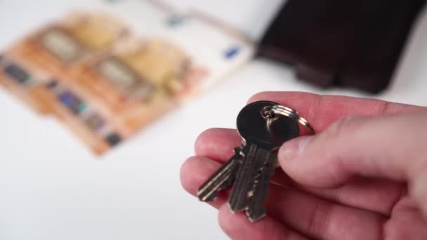 Lesklé nové klíče od bytu v ruce muže s eurobankovkami a peněženkou na bílém pozadí. Nákup nebo pronájem bytu v realitní kanceláři
