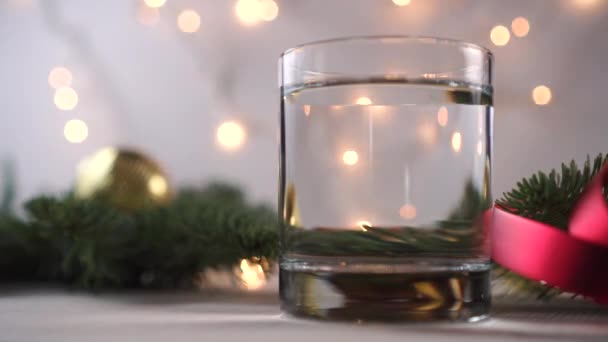 액체가 두꺼운 바닥을 유리잔이 반짝이는 갈랜드 가문비나무 장식등을 배경으로 크리스마스 — 비디오