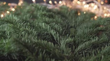 Bir adam, parlak kırmızı bir kurdele takıyor, bir Noel ağacının gür dallarına, yanıp sönen bir çelengin arka planına, bulanık sarı ışıklarla. Neşeli, canlı bir manzara.
