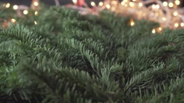Parlak kırmızı dekoratif kurdele, göz kırpan bir çelenk ve bulanık sarı ışıklarla, Noel ağacının yemyeşil dallarında sarmal halkalarda güzelce yerleştirilmiştir. Şenlikli, parlak manzara