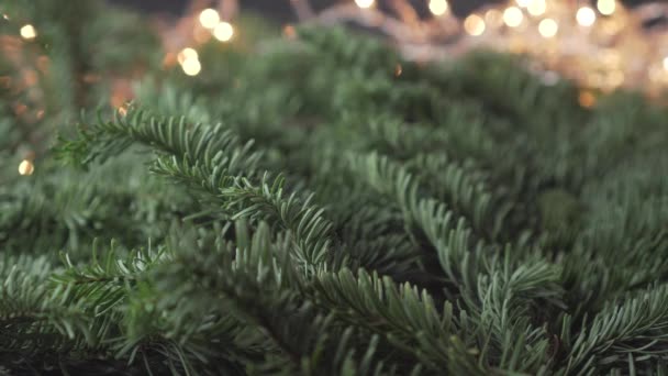 一个男人在绿油油的圣诞树枝条上挂着一个银白色的装饰球 背景是一个闪烁着黄光的模糊的花环 喜庆的风景 — 图库视频影像